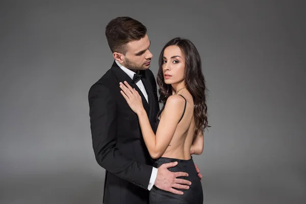 Atractiva pareja elegante en ropa negra abrazo aislado en gris - foto de stock