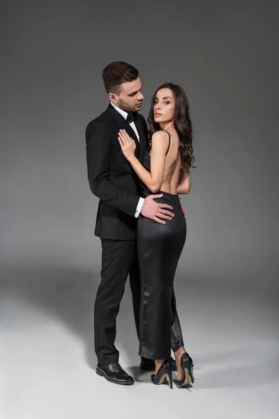 Schöne elegante Paar in schwarzen Kleidern umarmen auf grau — Stockfoto