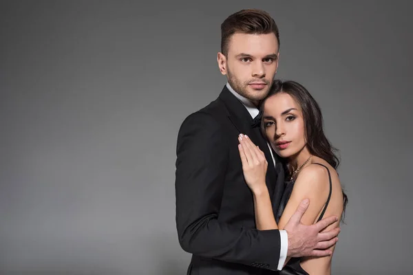 Elegantes Paar in schwarzer Kleidung umarmt sich vereinzelt auf grau — Stockfoto