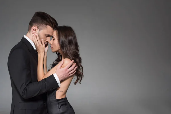 Tierna pareja elegante en ropa negra abrazando con los ojos cerrados aislados en gris - foto de stock
