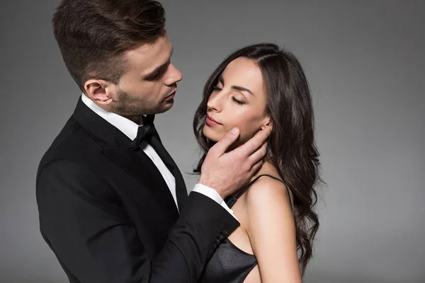 Attraktives elegantes Paar in schwarzer Kleidung, das sich isoliert auf grau umarmt — Stockfoto