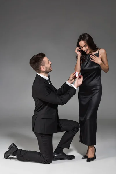 Young boyfriend holding proposal ring in box for attractive girlfriend on grey — Stock Photo