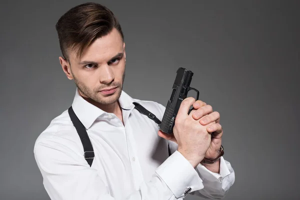 Красивий секретний агент з кобуром, тримає пістолет, ізольований на сірому — стокове фото