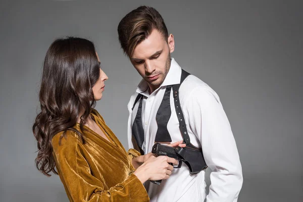 Attractive woman in golden dress taking gun from holster of secret agent, isolated on grey — Stock Photo