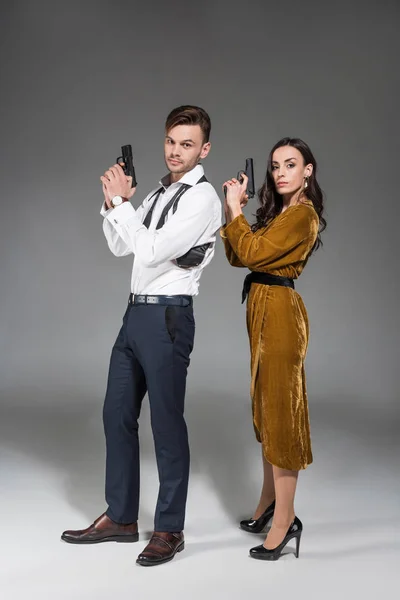 Hermosa pareja segura de agentes secretos posando con arma de fuego en gris - foto de stock