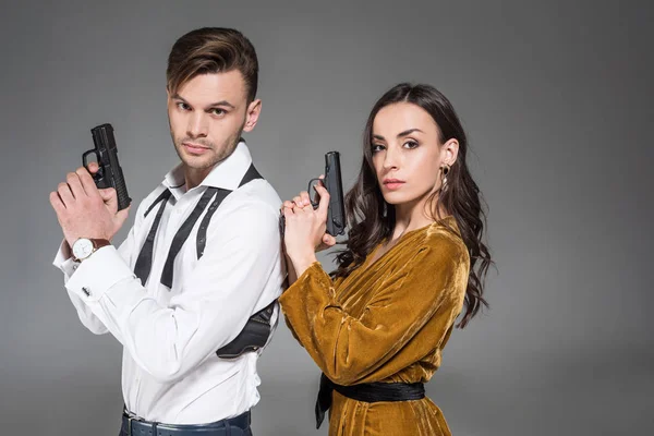Beautiful confident couple of secret agents posing with weapon, isolated on grey — Stock Photo