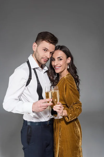 Young smiling couple hugging and holding champagne glasses isolated on grey — Stock Photo