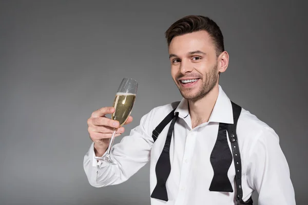 Hombre sonriente guapo sosteniendo copa de champán aislado en gris — Stock Photo