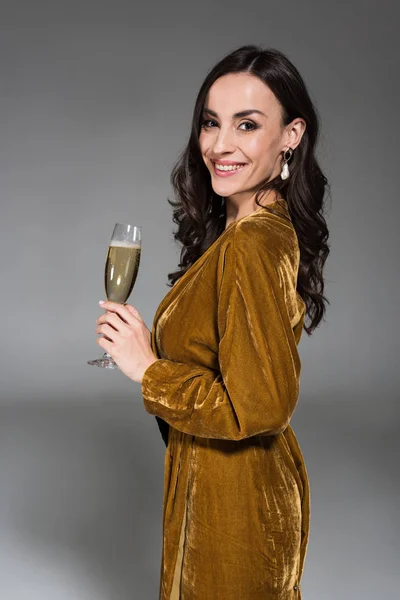 Hermosa mujer sonriente en vestido de oro sosteniendo copa de champán aislado en gris - foto de stock
