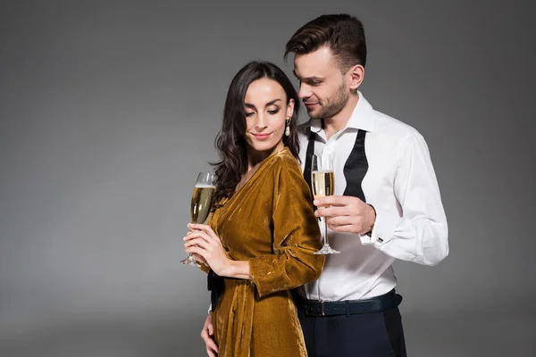 Young happy couple hugging and holding champagne glasses isolated on grey — Stock Photo
