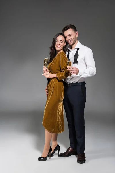 Couple souriant étreignant et tenant des verres à champagne sur gris — Photo de stock