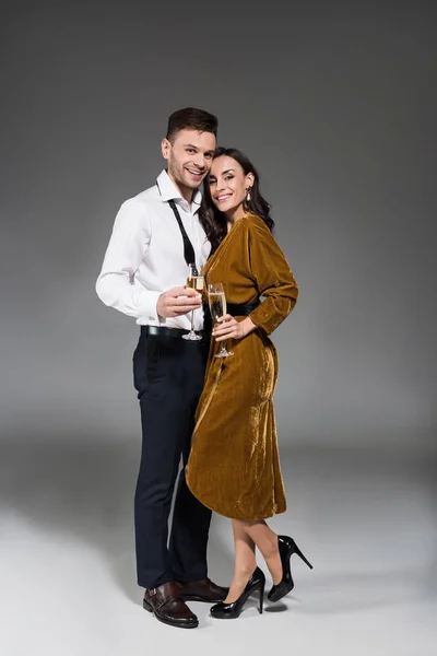 Young happy couple hugging and holding champagne glasses on grey — Stock Photo