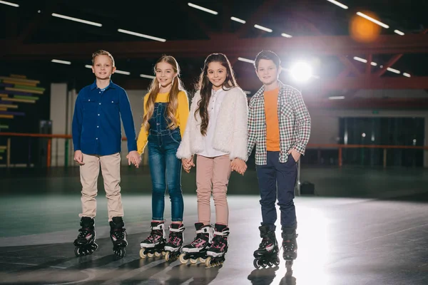 Mignons enfants souriants en patins à roulettes debout sur la patinoire spacieuse — Photo de stock