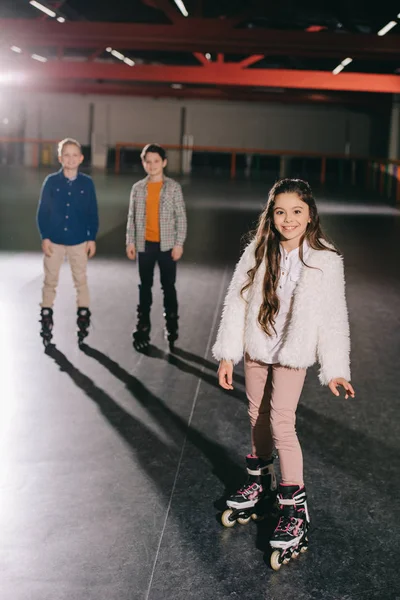 Foco seletivo de criança muito sorridente em patins com dois meninos no fundo — Fotografia de Stock