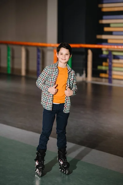Выборочный фокус милого улыбающегося мальчика в роликовых коньках, стоящего на просторном катке — стоковое фото