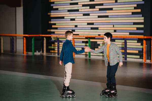 Красивые улыбающиеся дети на роликовых коньках, протягивающие друг другу руки — стоковое фото