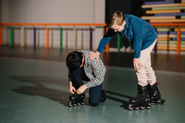 Pretty careful boy helping friend in fixing roller skate boot — Stock Photo