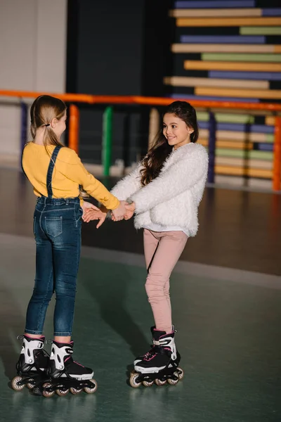 Niños bastante sonrientes en patines, de pie en una amplia pista de patinaje - foto de stock