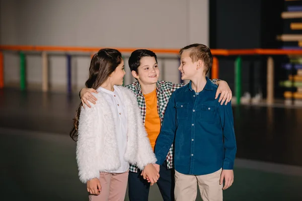 Niño bonito abrazando a dos amigos sonrientes con las manos cogidas - foto de stock