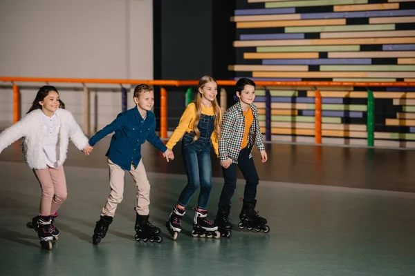 Grupo de crianças sorridentes patinando na pista de patins com as mãos dadas — Fotografia de Stock