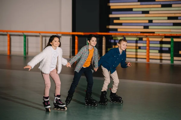 Three happy smiling children skating in roller rink with holding hands — Stock Photo