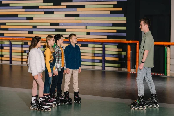 Enfants souriants en patins à roulettes écoutant les instructions des entraîneurs — Photo de stock