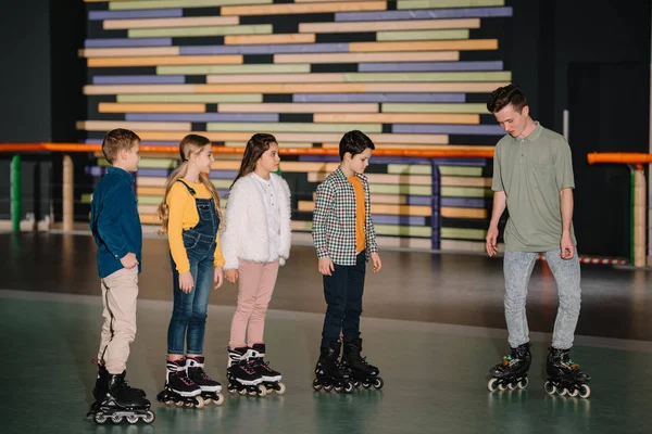 Young instructor showing skating poses to attentive children — Stock Photo