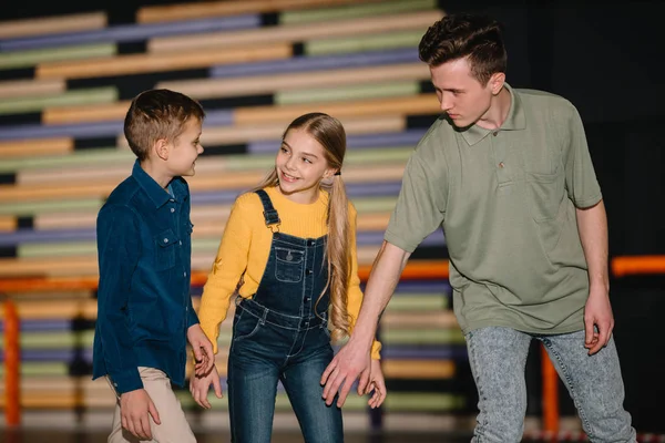 Foco seletivo de belo jovem treinador explicando técnicas de patinação para crianças sorridentes — Fotografia de Stock