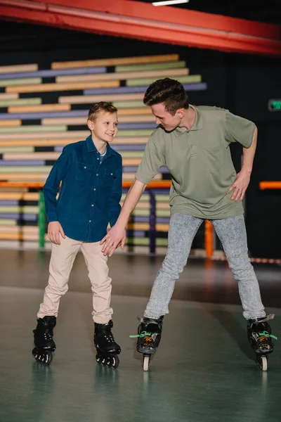 Schöner junger Trainer gibt lächelnden Jungen Anweisungen zum Schlittschuhlaufen — Stockfoto