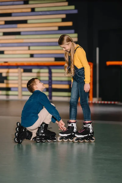 Выборочный фокус заботливого мальчика, помогающего улыбающемуся другу починить ботинок на роликовых коньках — стоковое фото