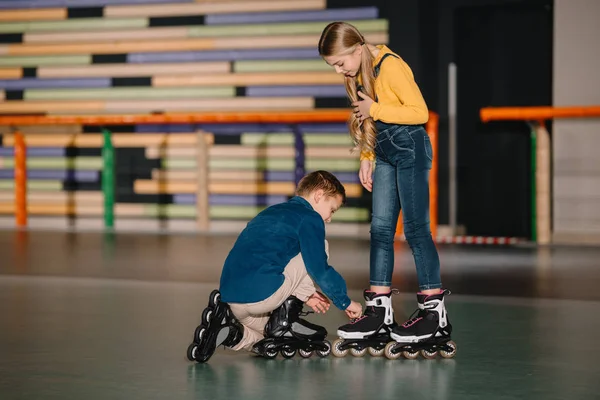 Осторожный мальчик помогает другу с ремонтом ботинок на роликовых коньках — стоковое фото