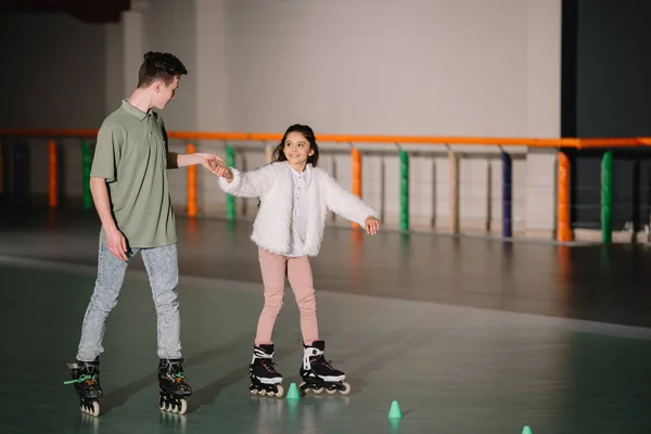Красивый инструктор держит ребенка на роликовых коньках, держа его за руку. — стоковое фото