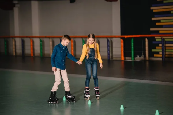 Two children practicing scating on rollers with holding hands — Stock Photo