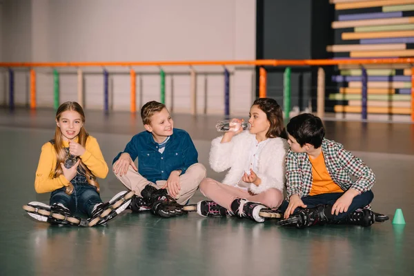 Children in roller skates drinking water on skating rink — Stock Photo