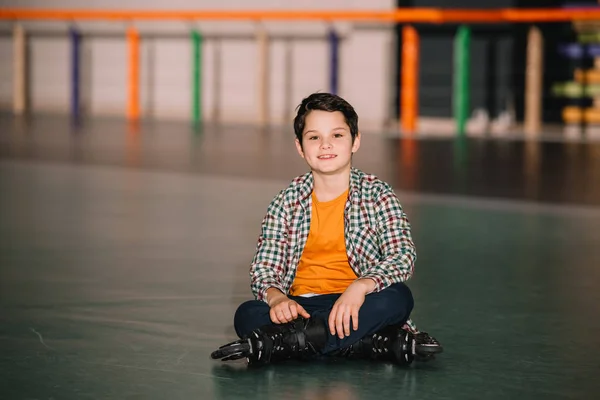 Brunette boy in roller skates sitting on roller rink — Stock Photo