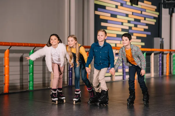 Four smiling kids holding hands while skating together — Stock Photo