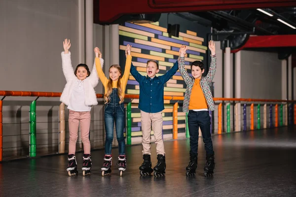 Cheerful kids in roller skates raising hands on skating rink — Stock Photo
