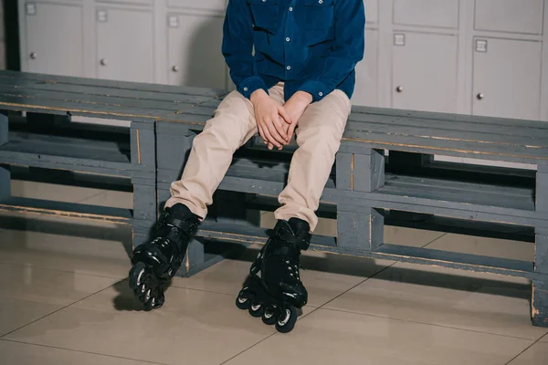 Tiro parcial de niño en patines negros sentado en el banco - foto de stock