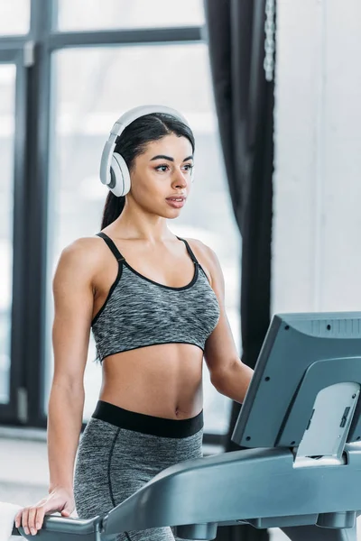 Beautiful sporty african american girl in headphones training on treadmill in gym — Stock Photo