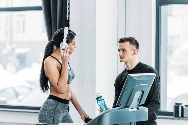 African american girl in headphones exercising on treadmill and looking at handsome young man in gym — Stock Photo