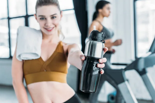 Vista de cerca de hermosa chica deportiva feliz sosteniendo botella de deportes con agua en el gimnasio - foto de stock