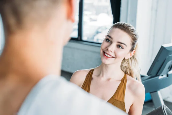 Cropped shot of smiling young sportswoman looking at man with towel on foreground in gym — Stock Photo