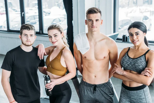 Multiracial group of sportive young friends standing together and smiling at camera in gym — Stock Photo