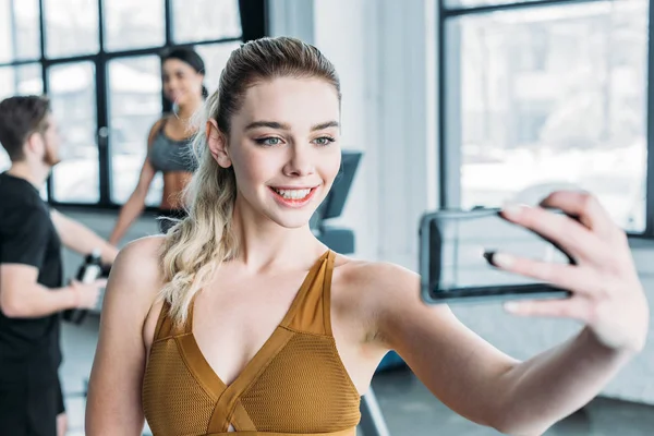 Schönes lächelndes sportliches Mädchen, das Selfie mit Smartphone im Fitnessstudio macht — Stockfoto
