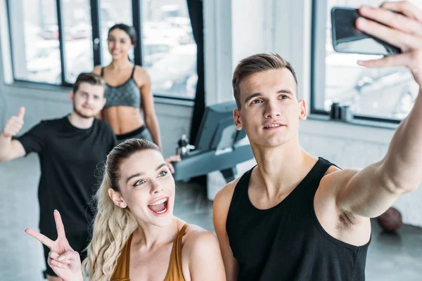 Multiethnic group of sportive young friends taking selfie with smartphone in gym — Stock Photo