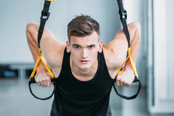 Schöner muskulöser junger Mann, der mit Federbeinen trainiert und im Fitnessstudio in die Kamera schaut — Stockfoto