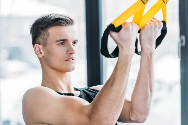 Schöner muskulöser junger Mann, der im Fitnessstudio mit Spanngurten trainiert — Stockfoto