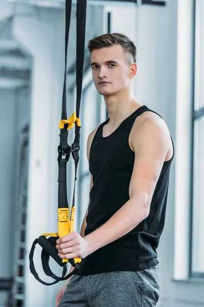 Handsome athletic man standing with resistance bands and looking at camera in gym — Stock Photo