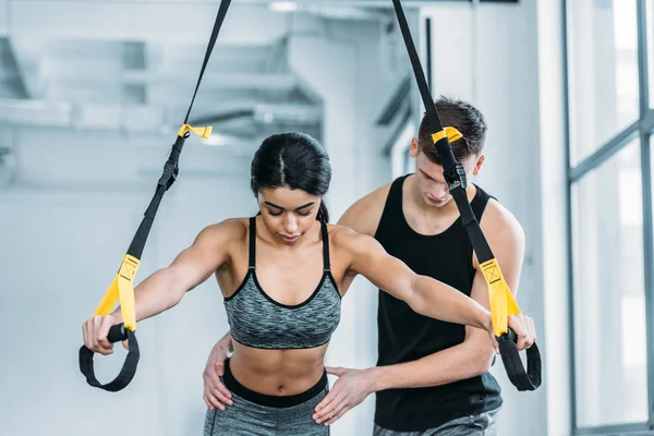 Trainer helping sporty african american girl exercising with resistance bands in gym — Stock Photo