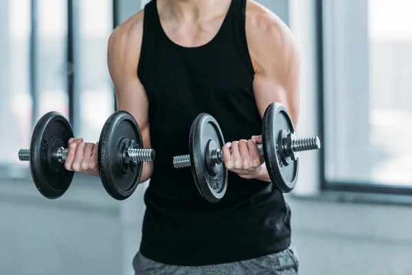 Cropped shot of muscular young man exercising with dumbbells in gym — Stock Photo